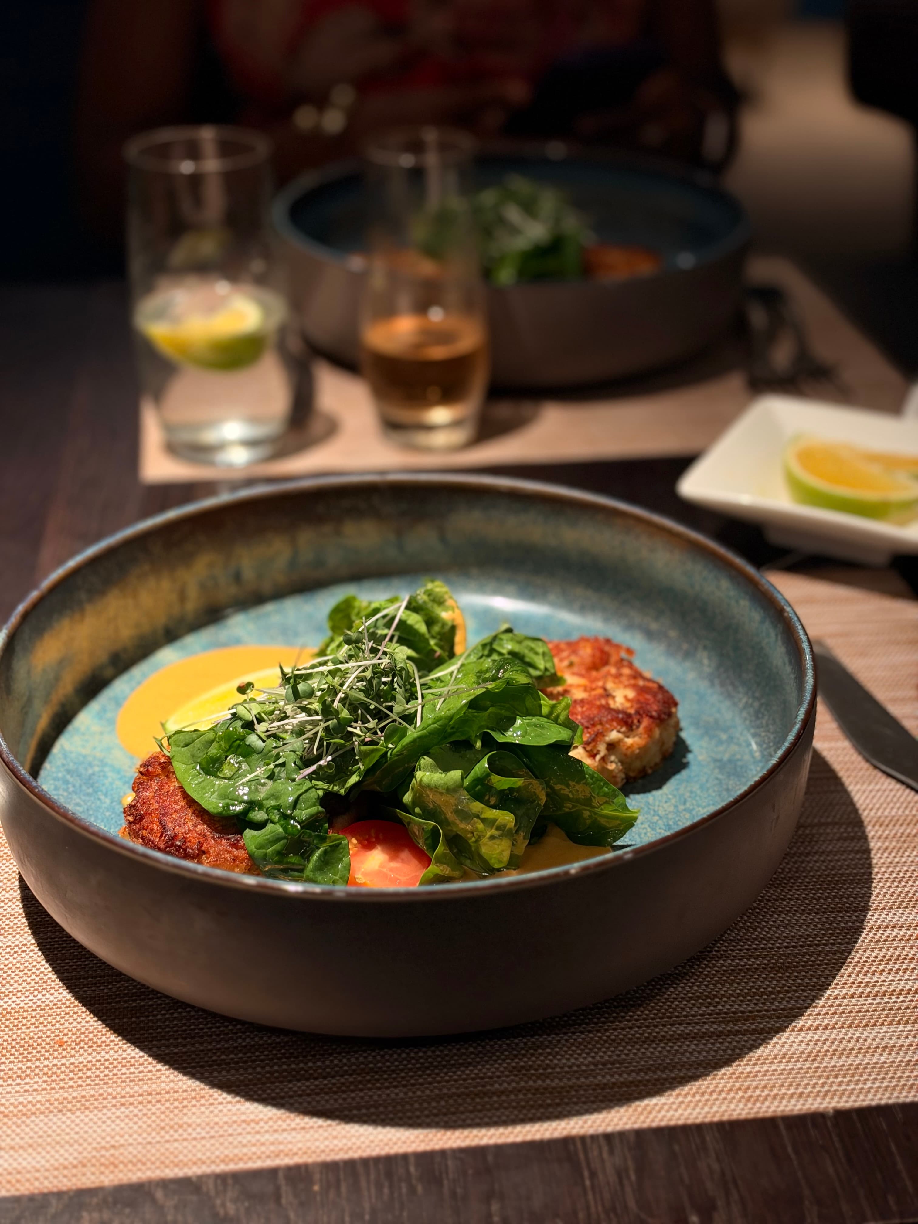 Crab cakes with spinach, tomato aioli, microgreens and lime in a blue bowl