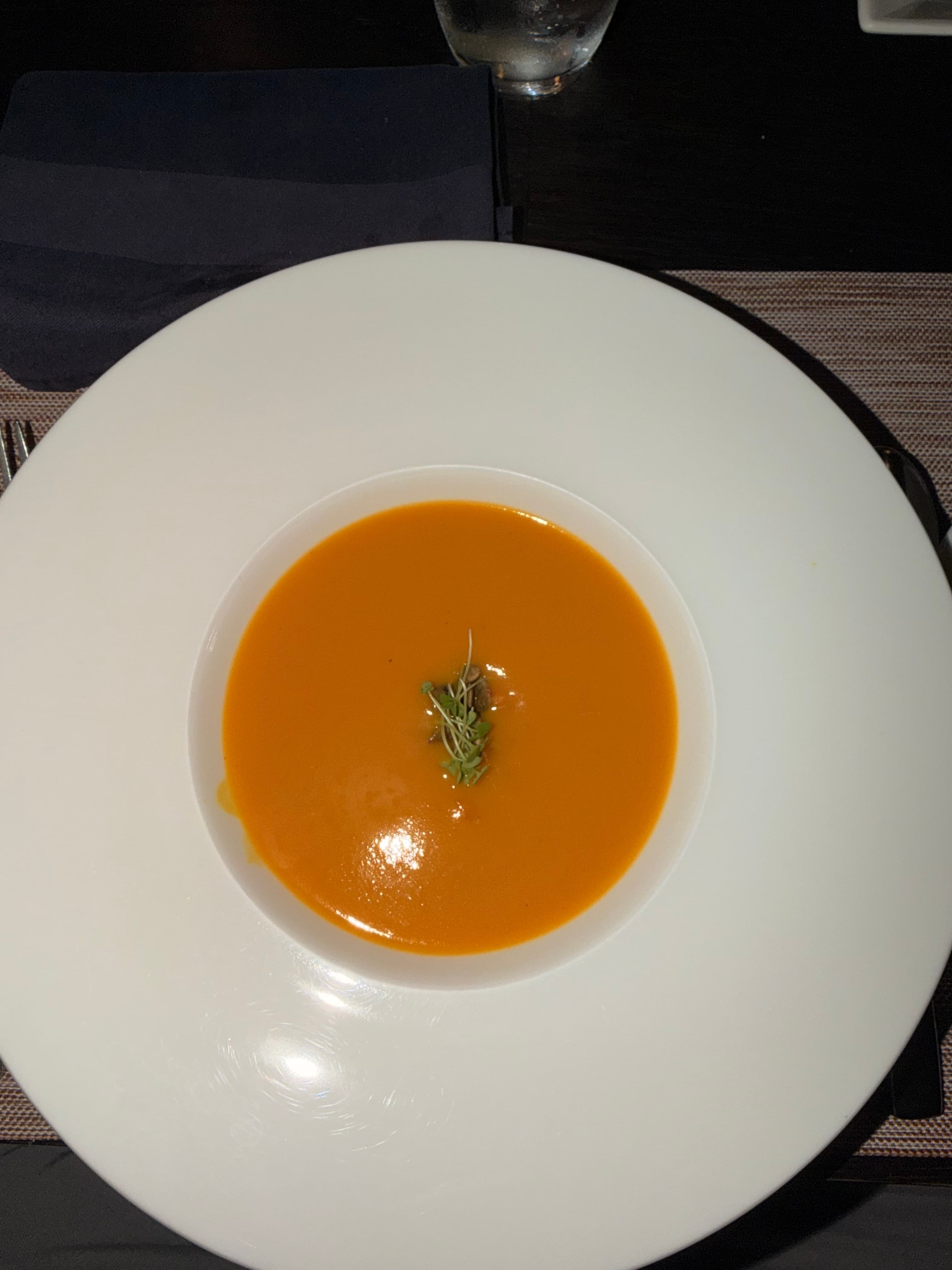 Orange pumpkin bisque with a small garnish in a white bowl